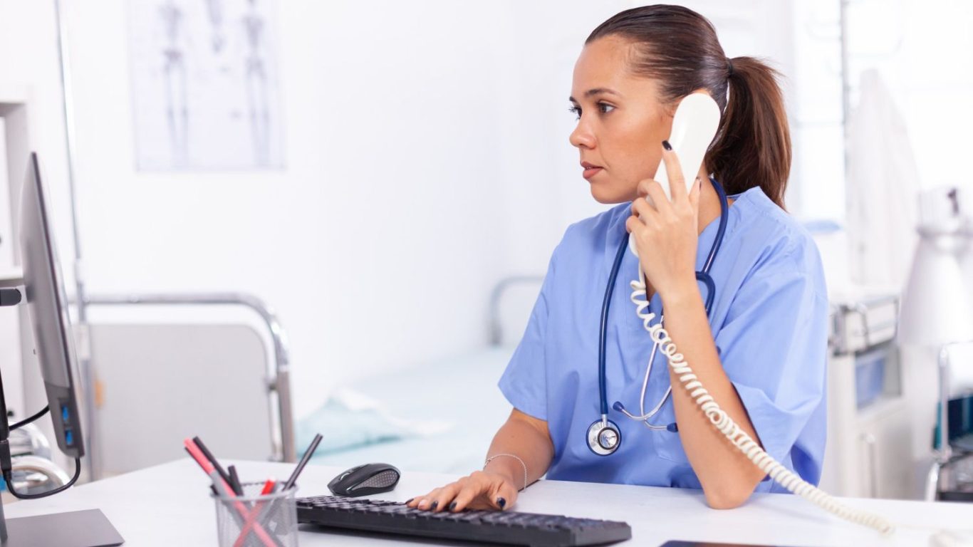 medical-nurse-talking-with-patient-phone-about-diagnosis-health-care-physician-sitting-desk-using-computer-modern-clinic-looking-monitor